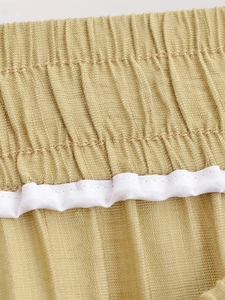 Détail de la texture plissée dorée et de la taille élastique blanche sur le pantalon décontracté
