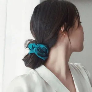 Detailed view of the dark peacock blue satin hair scrunchie styled in a low bun hairstyle