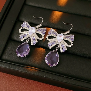 Close-up of bow earrings with purple teardrop gems and crystals in a jewelry box