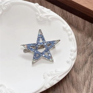 Detail of blue rhinestone star hair clip with silver metal base on a white vintage plate