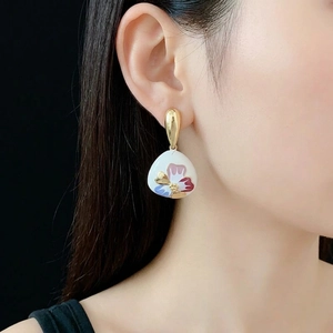 Vintage floral drop earrings with white enamel charms and gold accents on a model