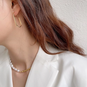 Detail of minimalist gold U-shape earrings and pearl twisted chain necklace on model