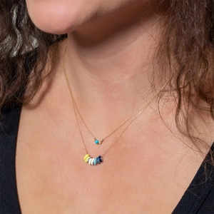 Close-up of double layer gold necklace with turquoise beads and colorful enamel charms