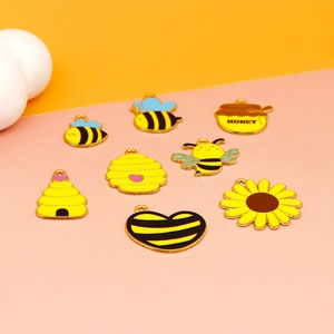 Macro shot of honey bee themed enamel charms including beehive and sunflower pendants