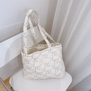 Detail of quilted white tote bag featuring red rabbit embroidery and french text label