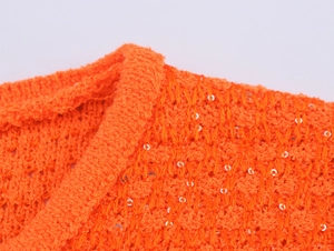 Detail von orangefarbenem Strickstoff mit silbernen Pailletten und weicher Textur
