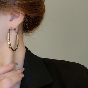 Close-up of a large polished silver hoop earring worn by a model in a black suit
