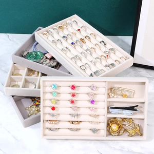 Beige velvet jewelry organizer trays for rings and watches stacked on marble surface