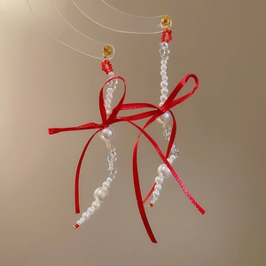 Macro detail of long pearl tassel earrings featuring large red ribbon bows and golden studs