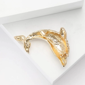 Macro shot of gold dolphin brooch with rhinestone texture on a white pedestal
