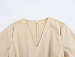 Gros plan détaillé de l'encolure en V et des broderies sur cette robe couleur beige