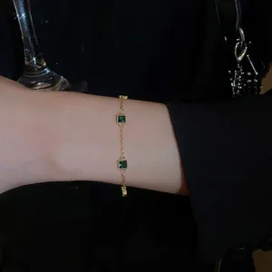 Bracelet élégant plaqué or avec pierres carrées vert émeraude porté par un mannequin chic