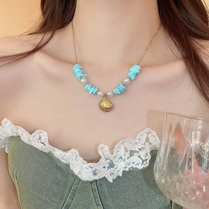 Close-up of a gold starfish shell pendant necklace with blue stones and pearls on a model