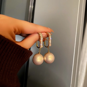 Boucles d'oreilles dorées avec perle rose clair et zircons blancs en gros plan à la main