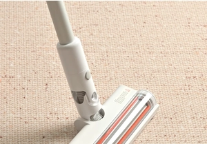 Close-up of a white electric vacuum cleaner head with orange brush on a beige carpet