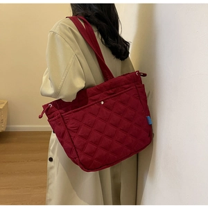 Detail of burgundy quilted tote bag with soft texture and side blue label on shoulder
