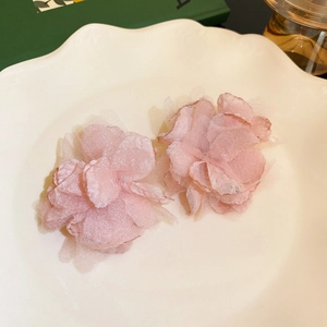 Close-up of pink tulle flower earrings with pearl accents on a white shell-shaped ceramic plate