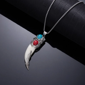 Macro detail of retro wolf tooth pendant with red gemstone and turquoise inlay on silver chain