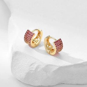 Close-up of golden huggie earrings with pave-set ruby-colored zircons on white stone