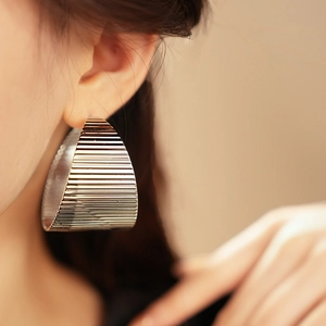Close-up of oversized silver geometric earrings with horizontal textured finish on a model