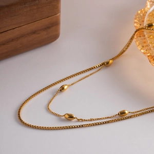 Detailed macro view of a gold double-layer necklace with box chain and oval beads