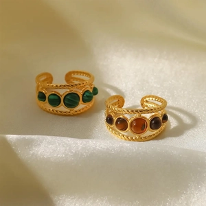 Dettaglio di anelli dorati con malachite verde e agata marrone su seta bianca pura