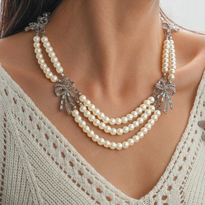 Close-up of elegant multilayer faux pearl necklace with rhinestone bow details on model