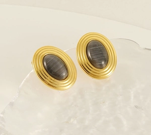 Détail de boucles d'oreilles ovales dorées avec pierre œil-de-chat grise sur verre poli