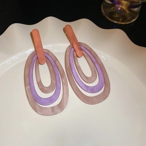 Detailed close-up of geometric resin earrings in purple and pink tones on a white ceramic plate