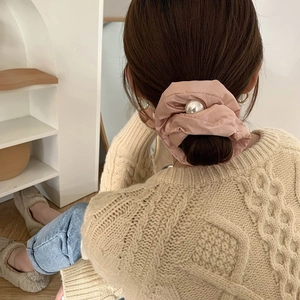 Pink satin scrunchie with large white pearl detail worn on hair with knit sweater