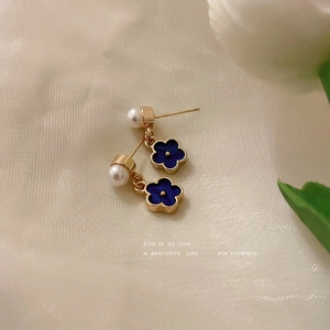 Elegant blue flower earrings with pearls and gold trim on soft white fabric