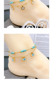 Close-up of double-layered gold anklet with turquoise beads, star and evil eye charms