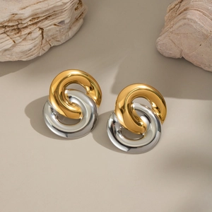 Minimalist interlocking gold and silver circle stud earrings on natural stone background
