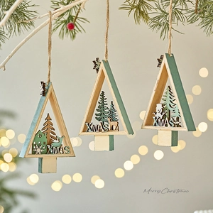 Three green wooden Christmas tree ornaments with laser-cut scenery hanging on pine branches