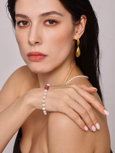 Détail d'un bracelet en perles d'eau douce avec gland et boucles d'oreilles dorées sur mannequin