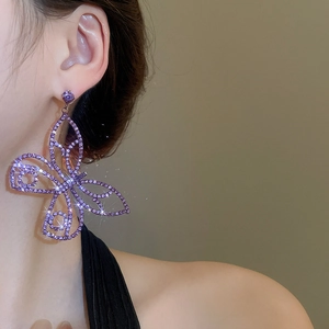 Close-up of a large purple butterfly earring with shimmering zircons on a model's ear