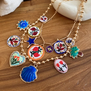 Golden beaded necklace detail with enamel sun, moon, and heart charms on wood surface