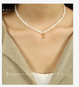 Detail of baroque pearl necklace with gold letter Z pendant worn on a beige sweater