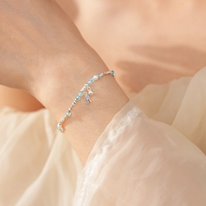 Close-up of silver beaded bracelet with white pearls and a blue fish charm on a wrist