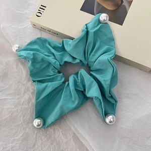 Detail of teal fabric hair scrunchie with four large white pearls on paper background