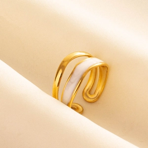 Close-up of dual-layer gold stainless steel and white enamel open ring on cream fabric