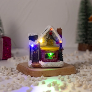 Close-up of a resin Christmas cabin with LED lights and snow-covered roof on a wooden base