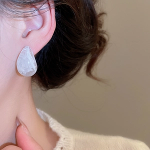 Close-up of teardrop resin stud earrings with white marble texture on a model ear