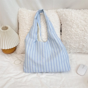 Detail shot of the blue and white striped canvas tote bag on soft white bedding