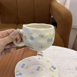 Hand-painted ceramic coffee cup with blue cherry pattern and irregular artistic edges