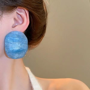 Close-up of large blue irregular round earring with textured finish worn by a model