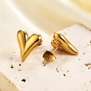 Macro shot of gold heart stud earrings on beige stone and silk background