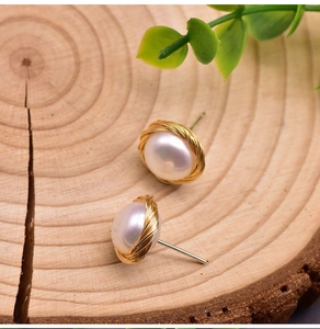Macro detail of button-style white pearl earrings with vintage golden wire wrapping