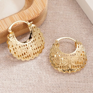 Detailed close-up of golden hollow flower hoop earrings on a beige textured background