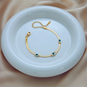 Gold snake chain bracelet with evil eye charms on champagne satin background